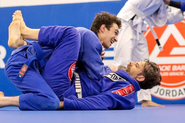 two male at a Brazilian Jiu jitsu classes one of them is smiling. On the background Gracie Barra West Jordan's logo.