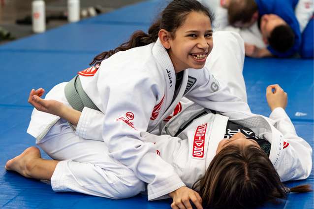 two teenagers practicing Brazilian Jiu Jitsu at Gracie Barra West Jordan, the girl is looking to the camera smiling.